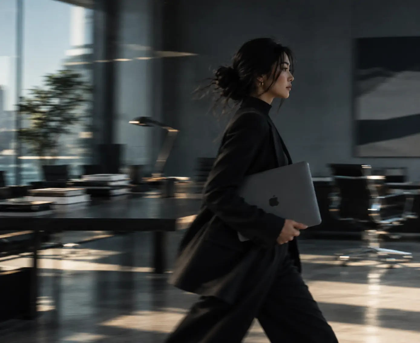 A businesswoman walking through an office with a laptop
